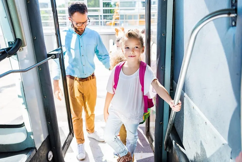 Liten flicka med rosa ryggsäck kliver på en buss.