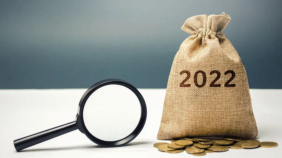 Pengasäck med texten 2022 på står på ett bord bredvid mynt och ett förstoringsglas.