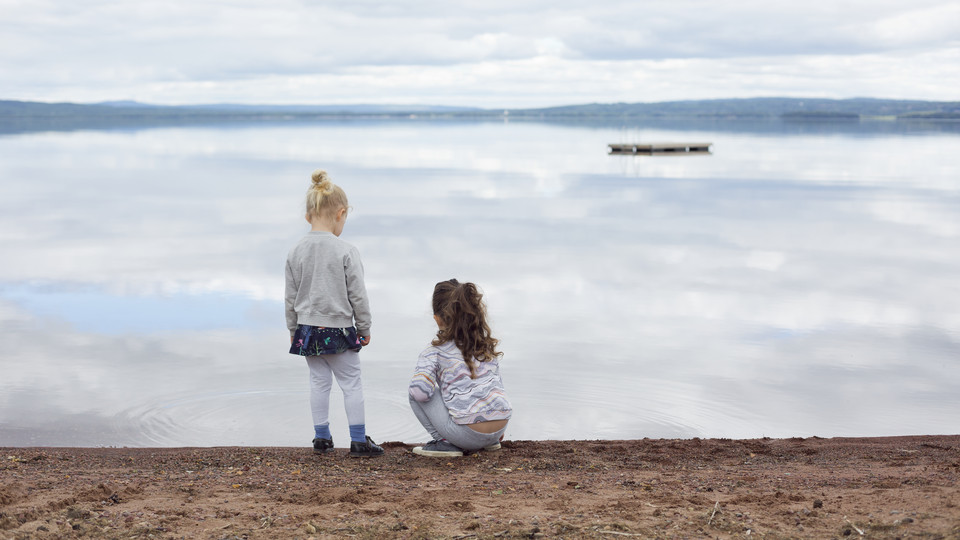 Två barn står på stranden och tittar ut över Orsasjön. Foto.