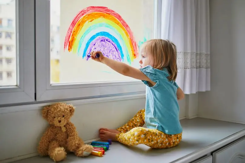 Barn målar regnbåge på fönster.