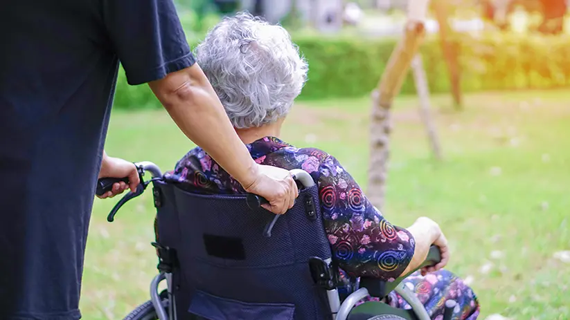Vårdpersonal skjutsar äldre kvinna i rullstol