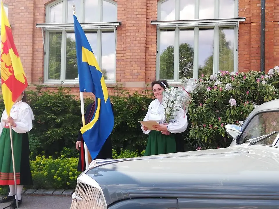 Anna-Karin Bengtar, årets kulturstipendiat har famnen full av blommor. Hon har orsadräkt på sig och står framför kommunhuset i Orsa.