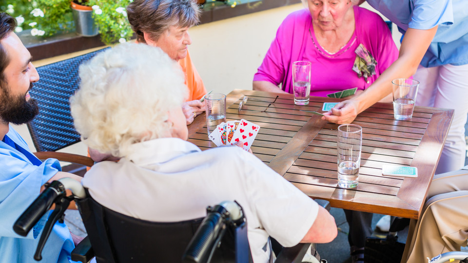Äldre spelar kort med sköterskorna på äldreboendet. 