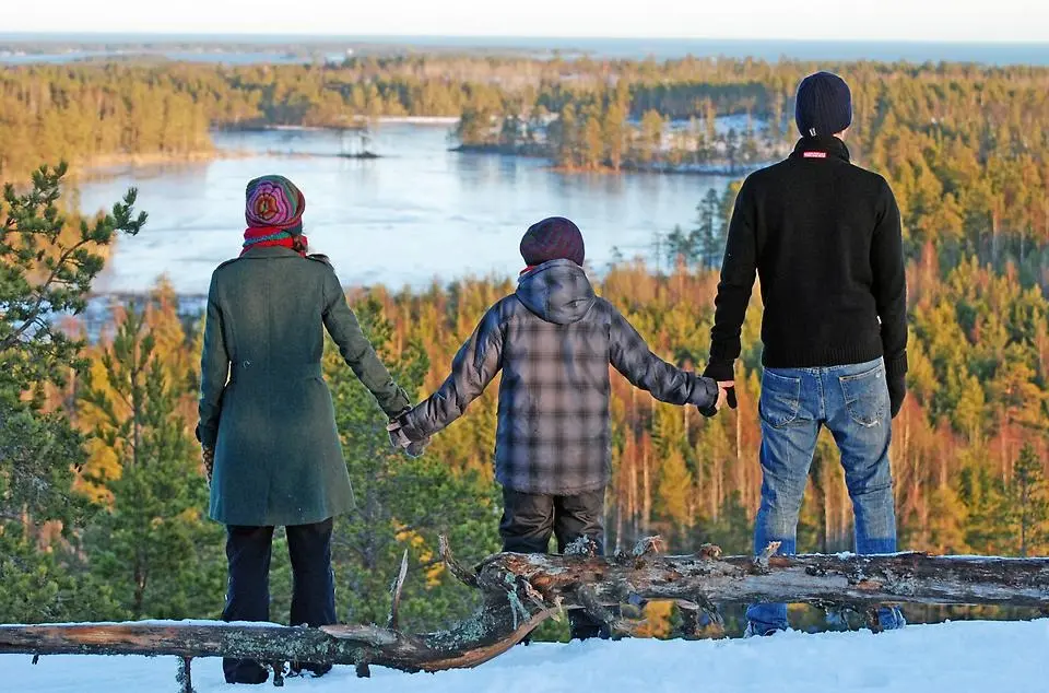 Familj står och håller varandras händer och tittar ut över sjö och skog.