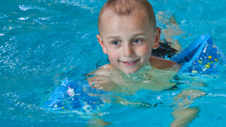 Pojke med armpuffar i simbassäng.