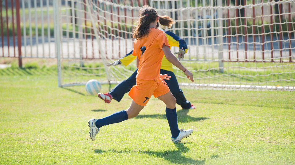 Tjejer spelar fotboll framför målet på en fotbollsplan. 
