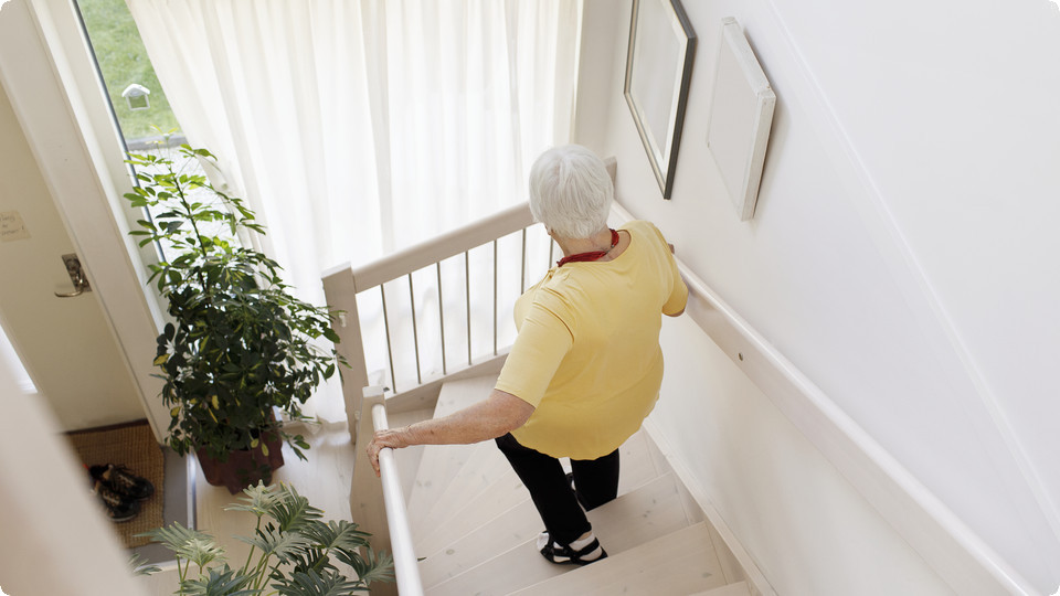 Äldre kvinna går nedför trappa i sitt hem