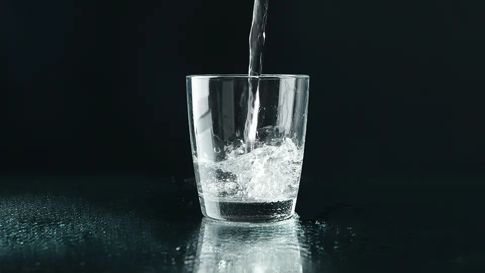 Vatten hälls i ett glas, svart bakgrund