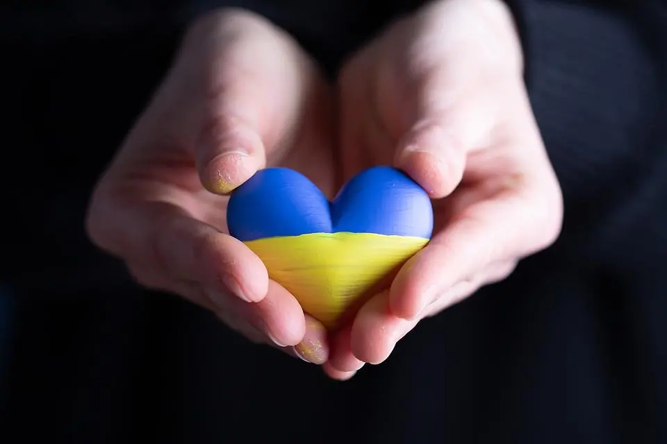 Två händer håller i ett litet hjärta i ukrainska färgerna blått och gult. Foto.