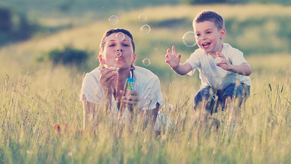 En kvinna och en pojke ligger på en äng och blåser såpbubblor. Foto.