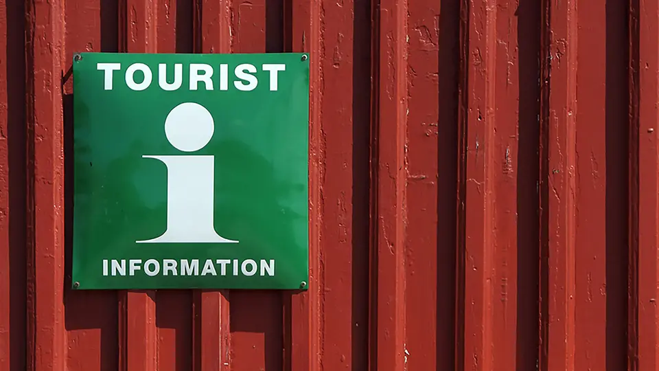 Grön skylt där det står Tourist information på röd trävägg
