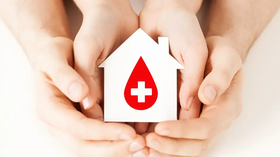En vuxen hand håller ett barns hand. De håller ett miniatyrsjukhus med ett rött kors i sina händer. Foto.