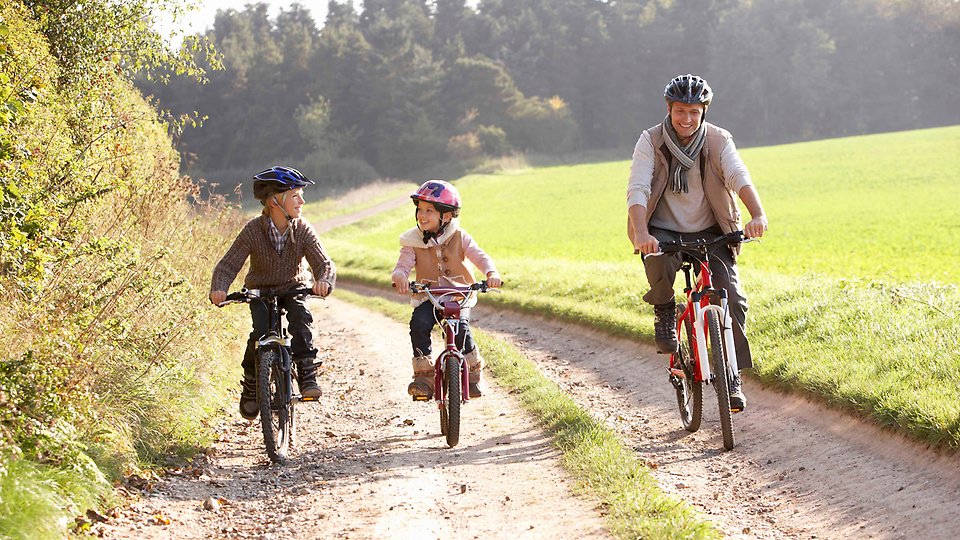 Pappa och två barn som cyklar på en grusväg i höstlandskap