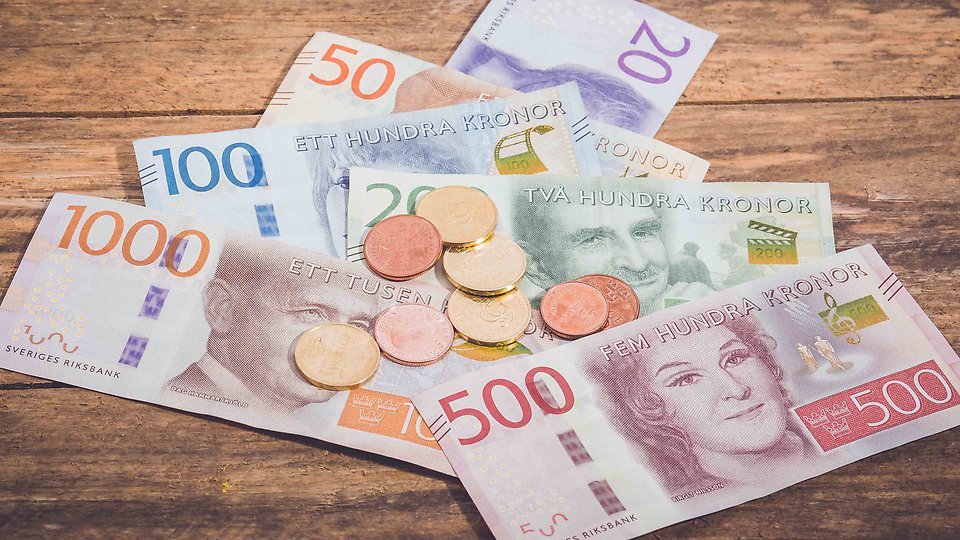 Svenska sedlar och mynt i olika valörer ligger utspridda på ett bord. Foto.