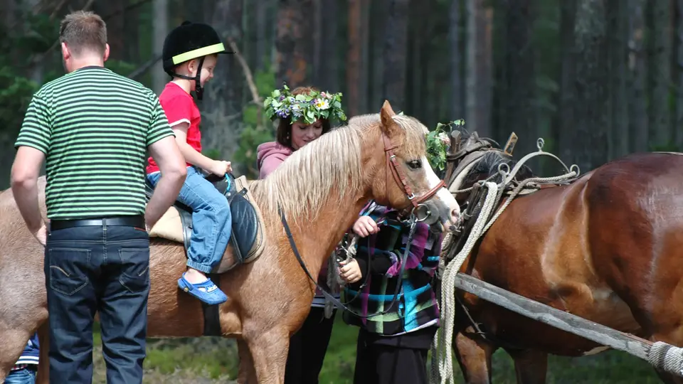 Liten pojke rider på häst, pappa och unga tjejer står bredvid